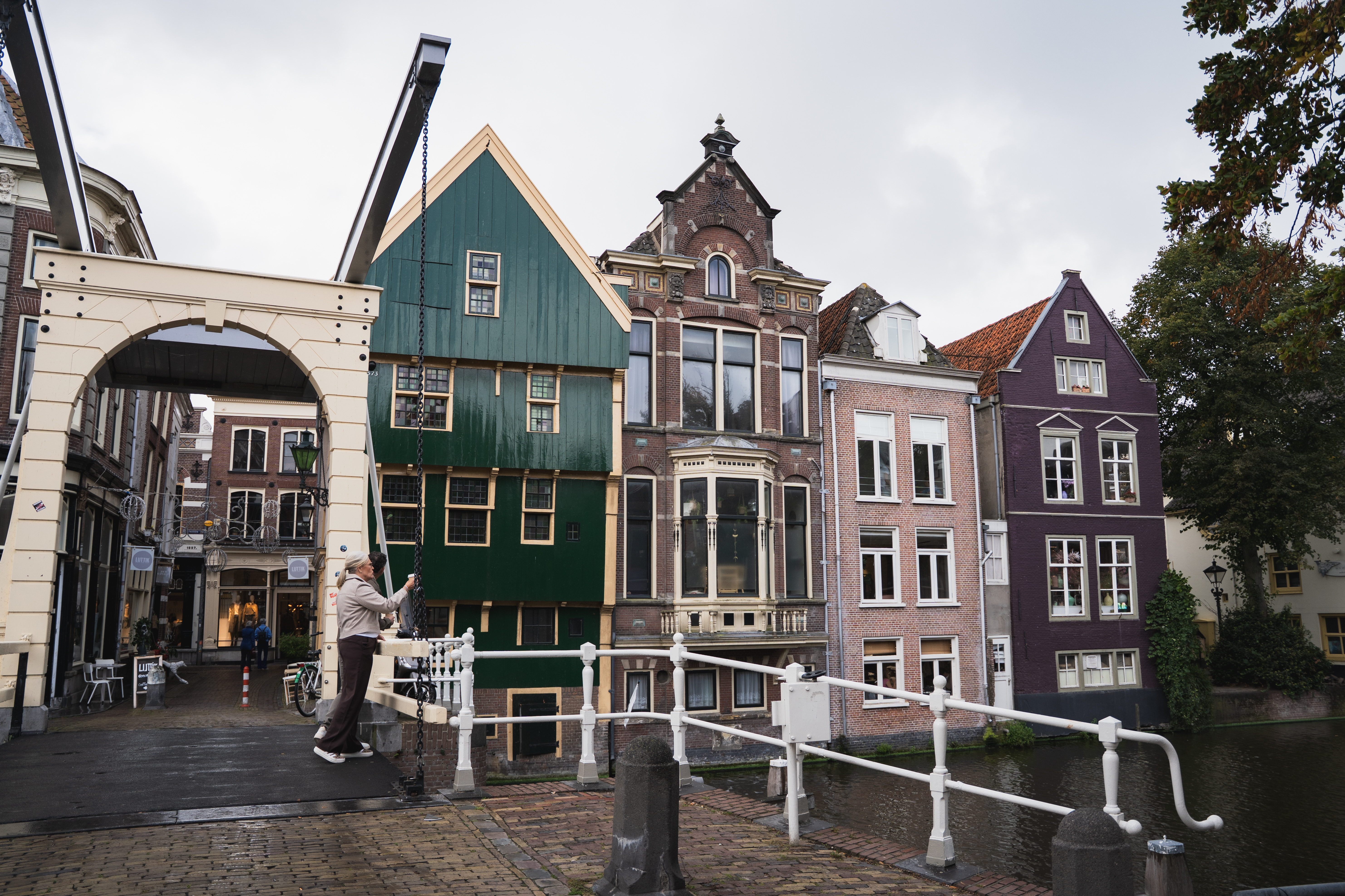 Man maakt foto van een gracht op een brug met grachtenpanden op de achtergrond